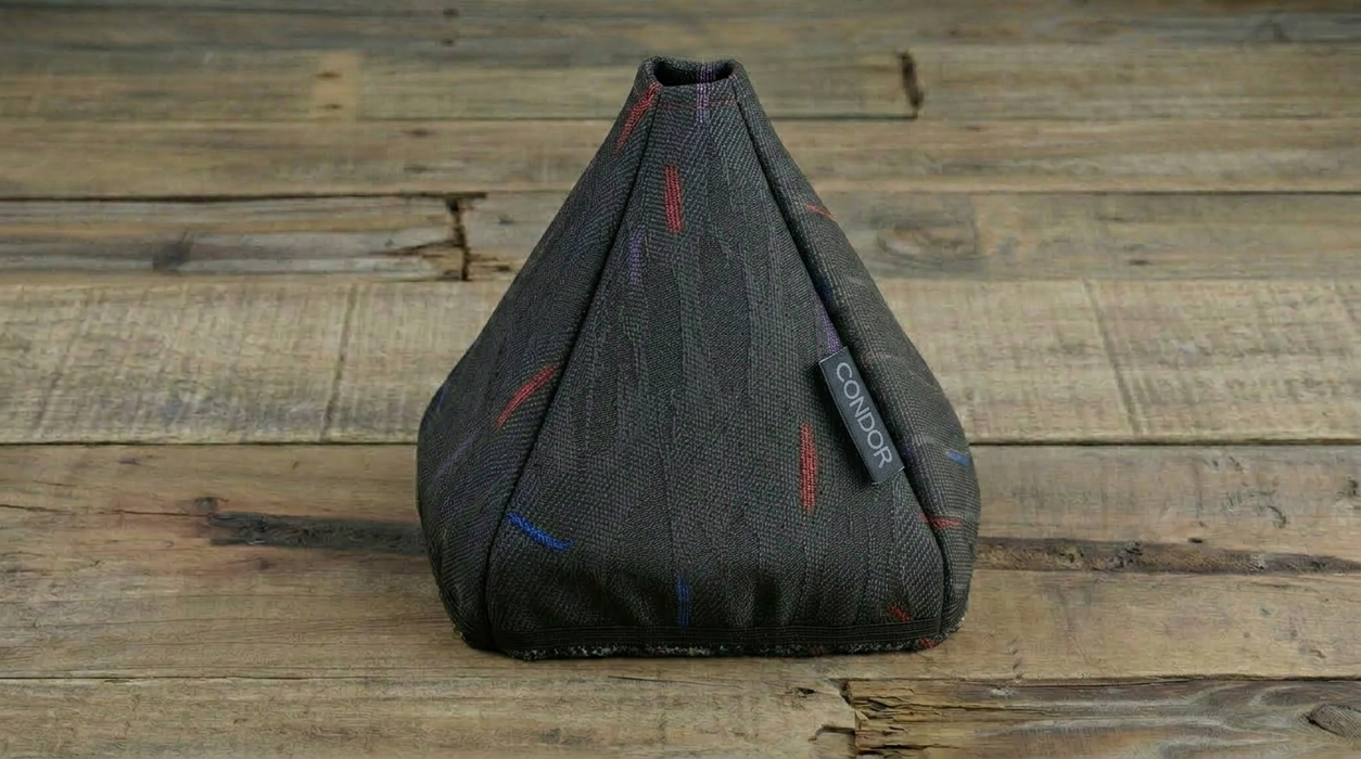 A dark gray textured car gear shift boot cover with small red and blue embroidered accents, resting on a rustic wooden plank surface.