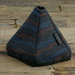 A triangular fabric cover with a dark gray base and thin blue and orange stripes, resting on a rustic wooden plank surface. A small black fabric tag on the side reads 'COOLGIRL'.