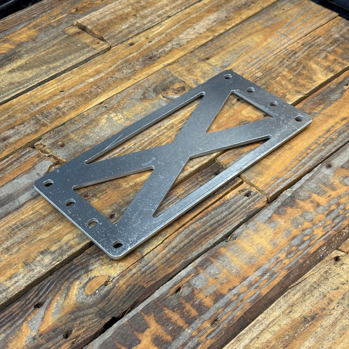 A dark gray metal license plate frame with a cutout X design, resting on a rustic wooden plank surface.