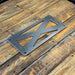 A dark gray metal license plate frame with a cutout X design, resting on a rustic wooden plank surface.