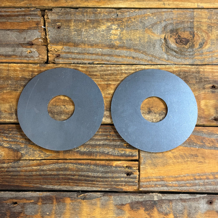 Two circular gray metal discs with central holes, placed side by side on a rustic wooden plank surface.
