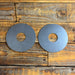 Two circular gray metal discs with central holes, placed side by side on a rustic wooden plank surface.