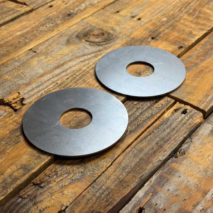 Two circular metal washers with center holes, displayed on a rustic wooden plank surface.