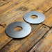 Two circular metal washers with center holes, displayed on a rustic wooden plank surface.
