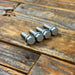 Four silver hex head bolts arranged in a row on a rustic wooden plank surface.
